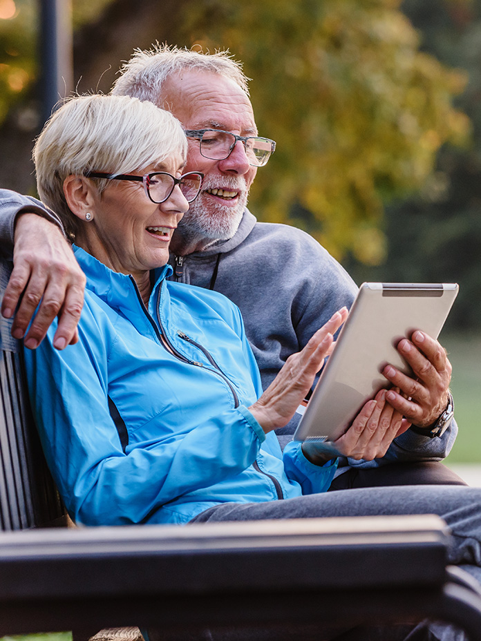 Image of an elderly couple sitting on a bench looking for Aetna Medicare plan coverage and benefits on a tablet