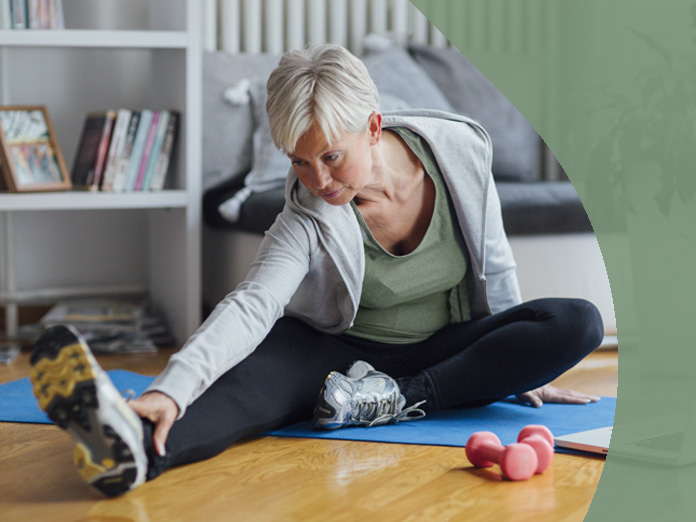 Woman stretching on a yoga mat in her home attending a SilverSneakers virtual fitness class